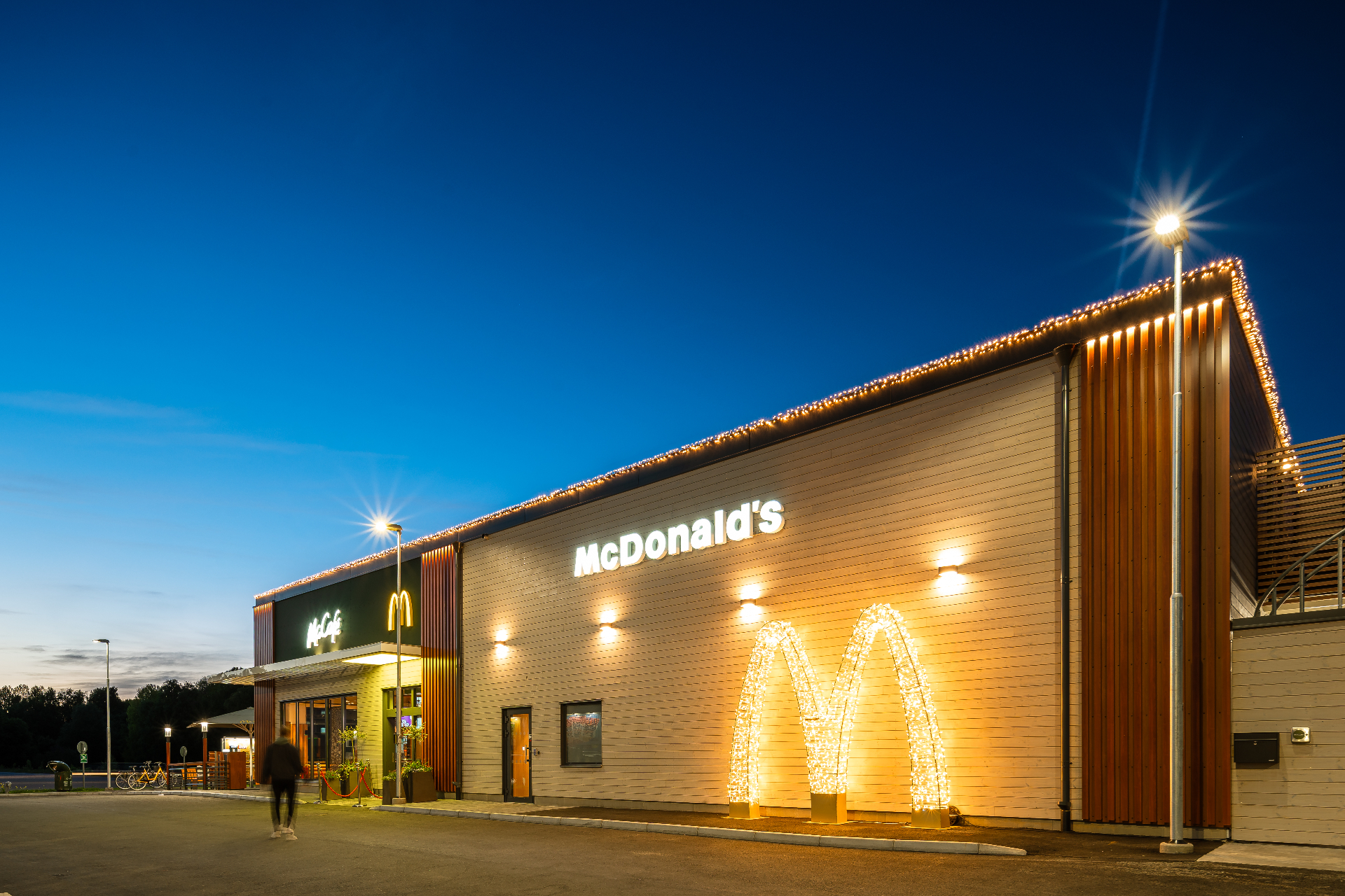 McDonald's Eksjö – långfasad med upplyst M-logotyp och takslingor mot djupblå himmel.