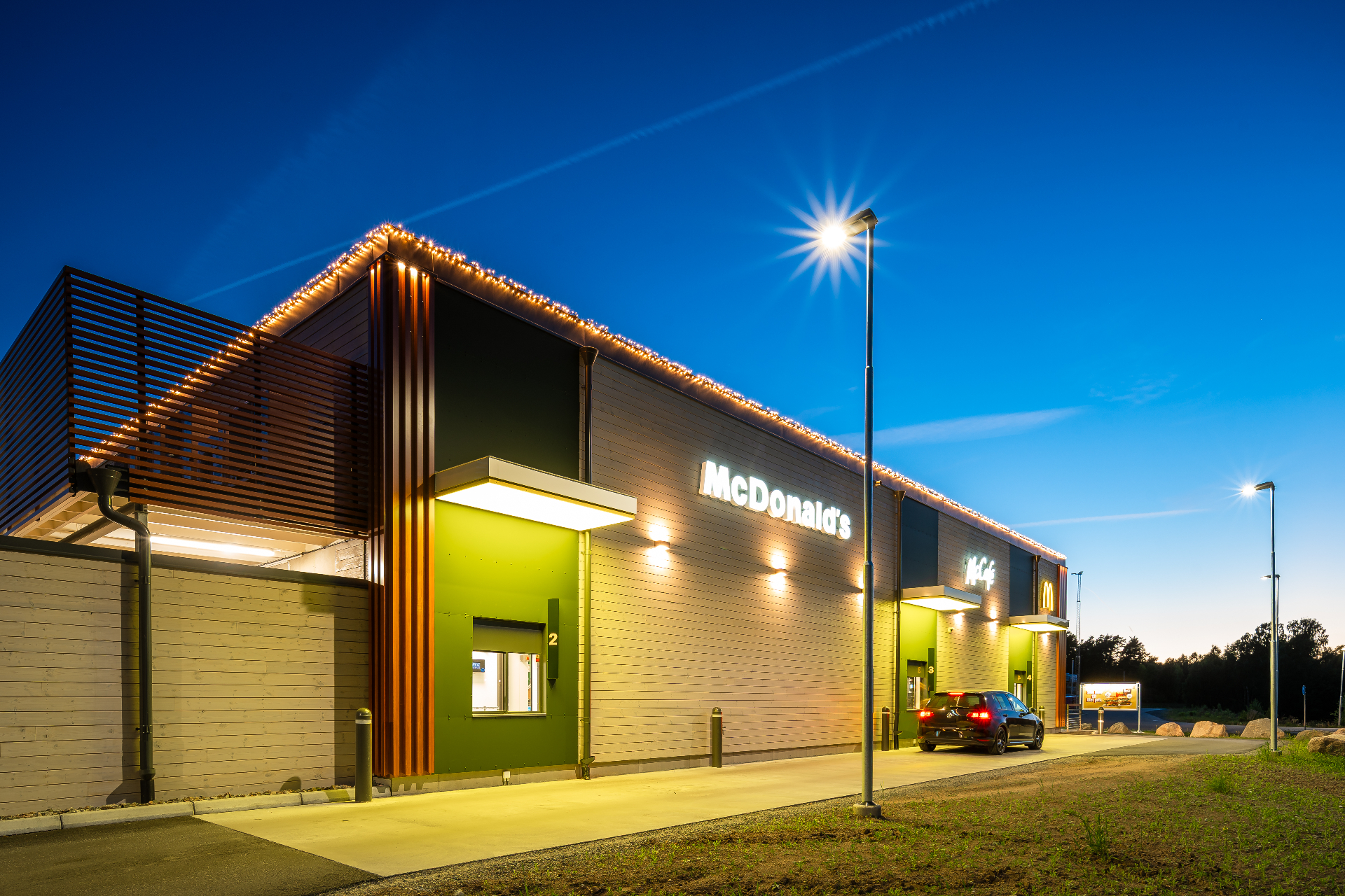 McDonald's Eksjö – drive thru-sidan med gröna paneler, träspjälor och varm fasadbelysning.