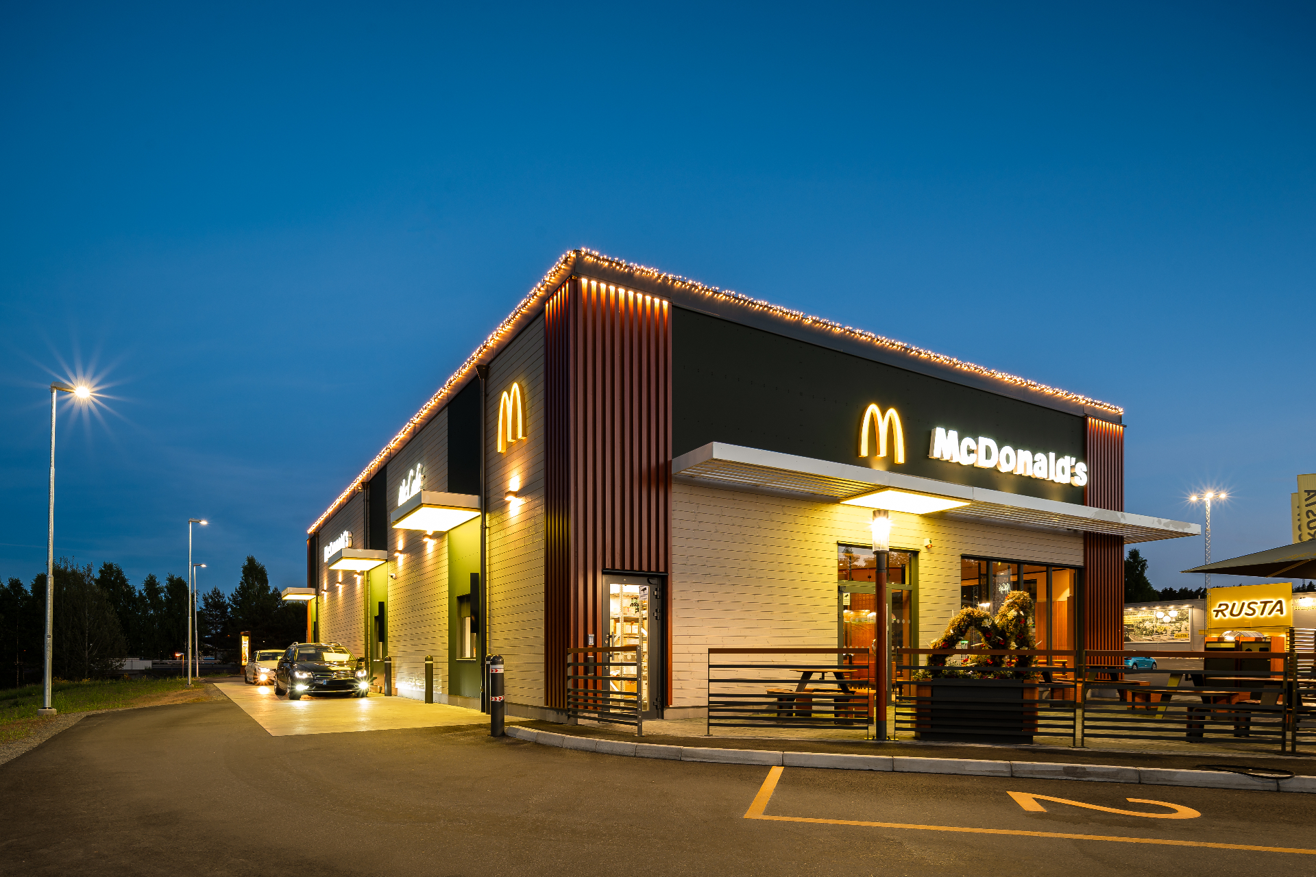 McDonald's Eksjö – hörnfasad med belysta takslingor och upplyst entré under blue hour.