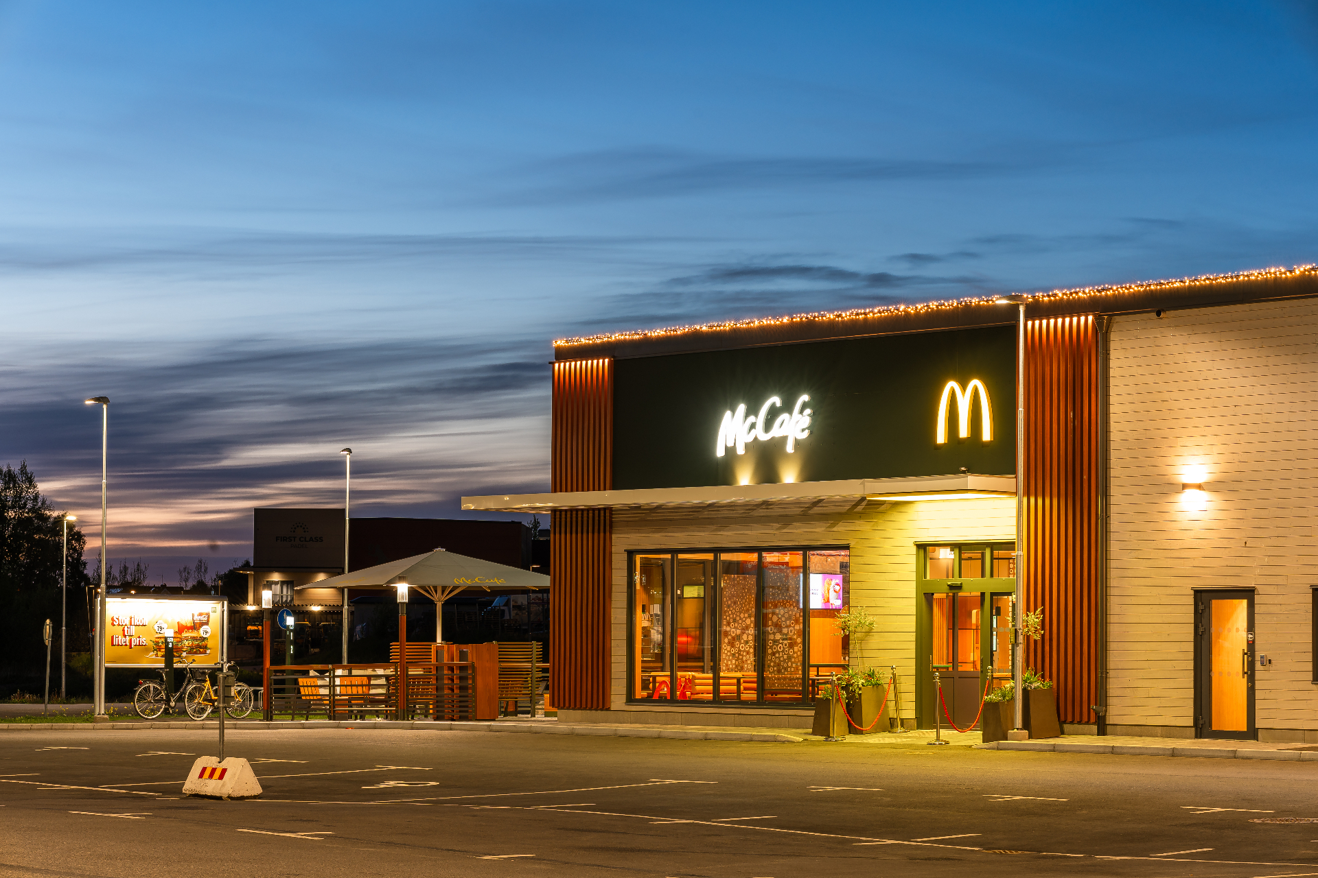 McDonald's Eksjö – McCafé-entré med parasoll och McCafé-skylt under kvällshimmel.