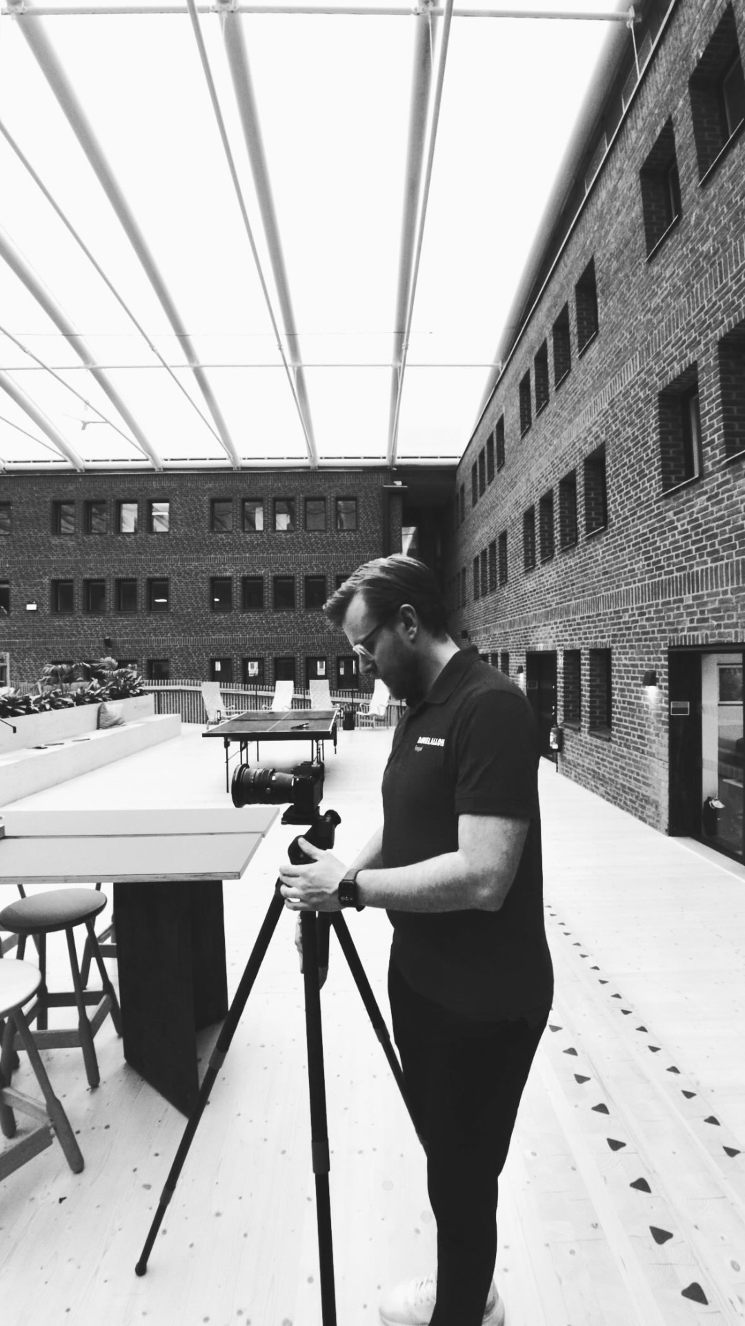 Daniel Alloh med kamera på stativ i ljust atrium med tegelfasader.
