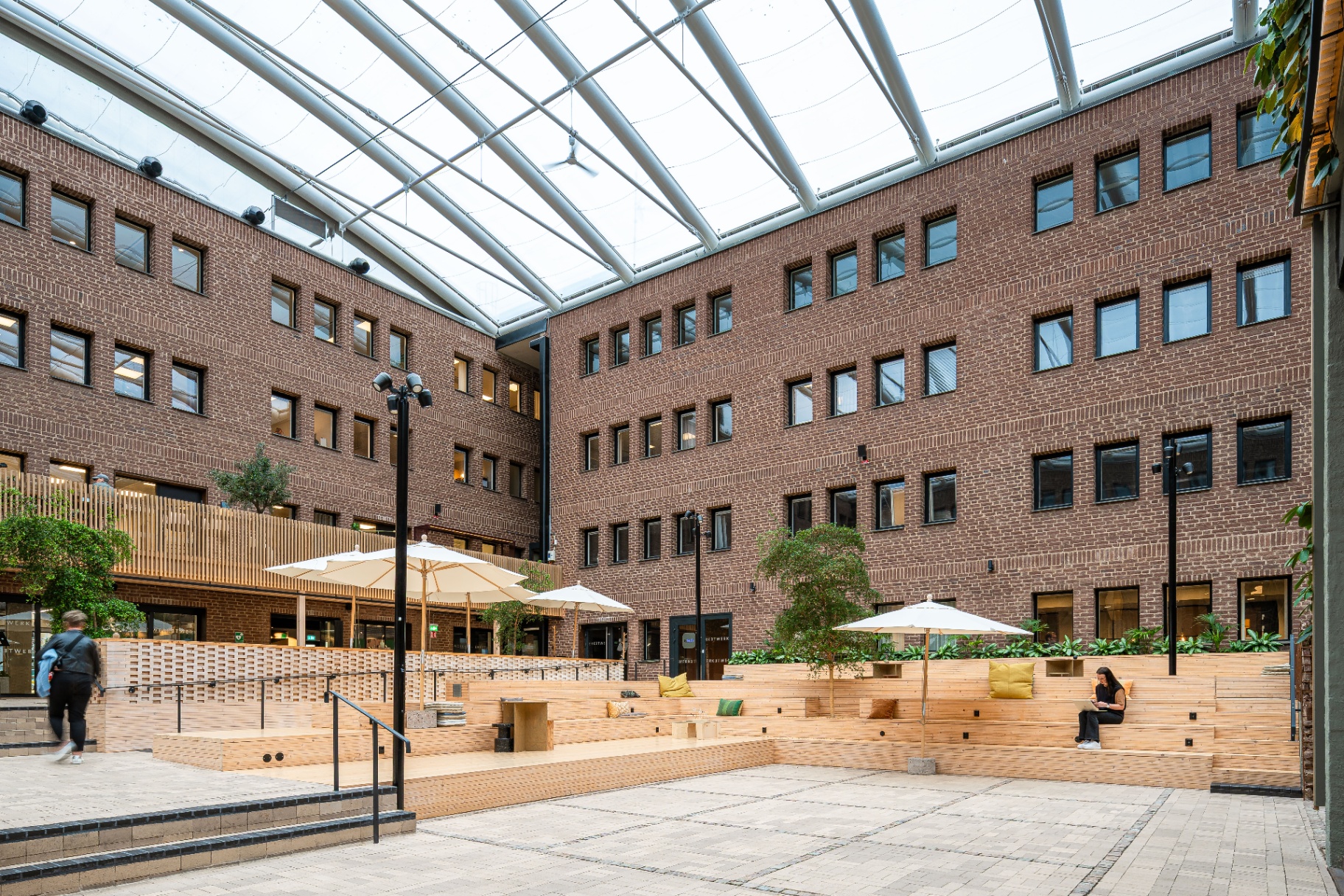 Werket Jönköping – innergård med tegelfasader, träläktare och parasoller under glastaket.