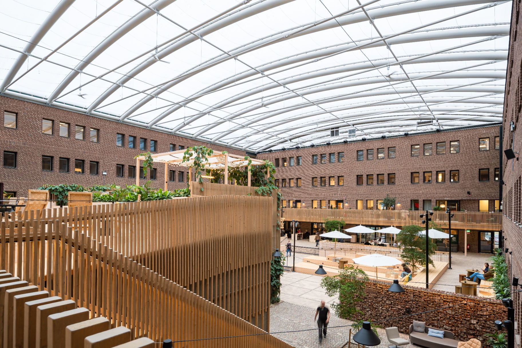 Werket Jönköping – överblick av glasöverbyggd innergård med tegelfasad, träarkitektur och grönska.